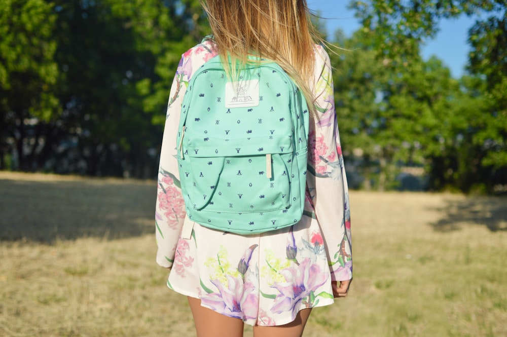 woman in white and multicolored floral long-sleeved mini dress with green backpack