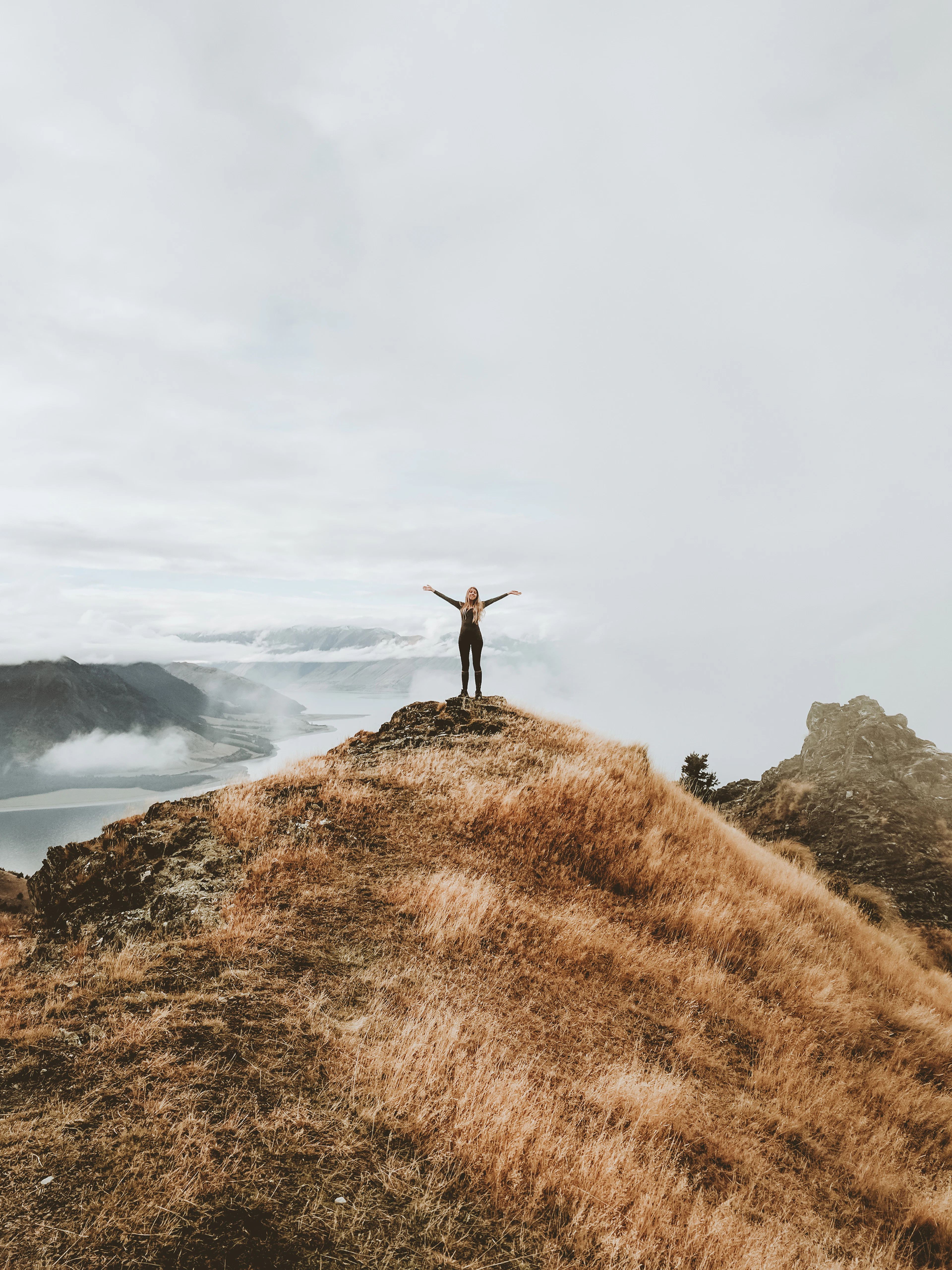 A person with arms raised on a hilltop above the clouds