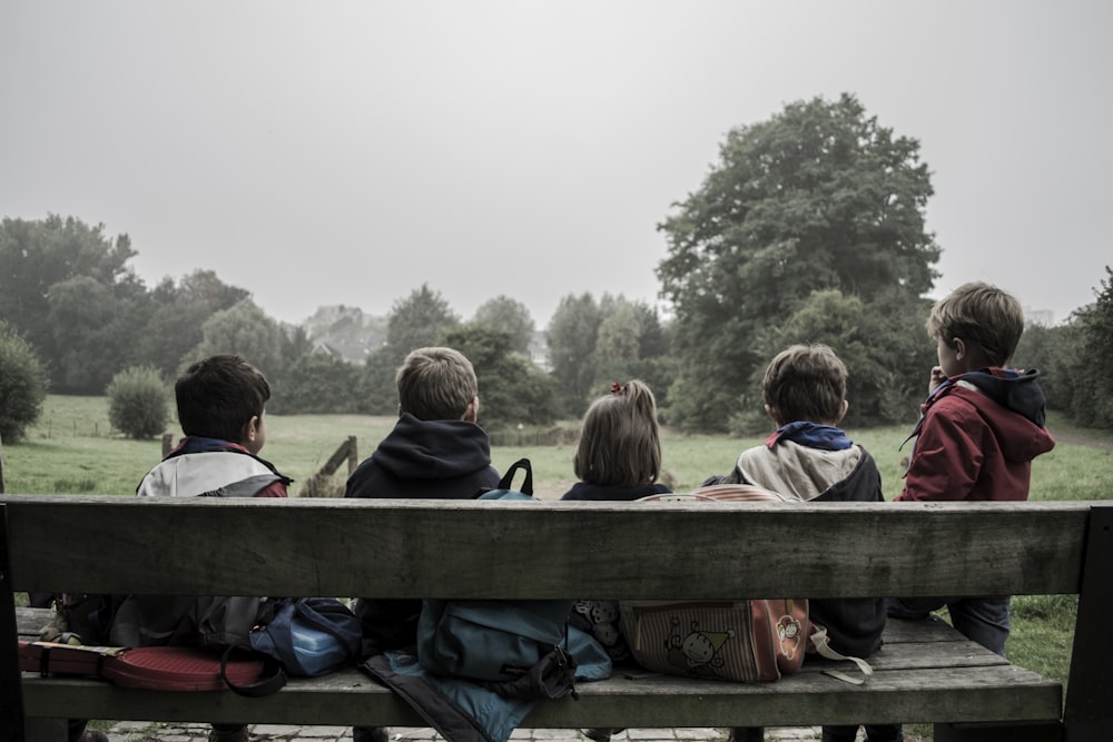 five children sitting on bench front of trees