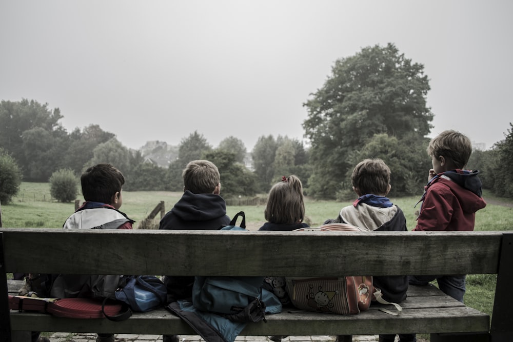 Fünf Kinder sitzen auf einer Bank vor Bäumen