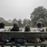 five children sitting on bench front of trees