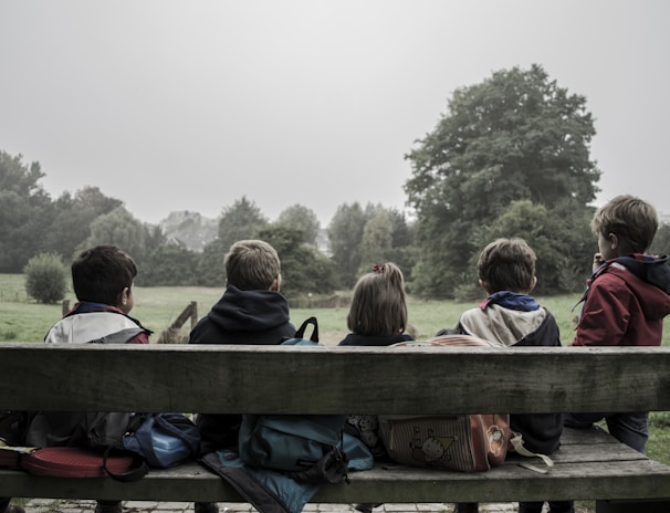 five children sitting on bench front of trees