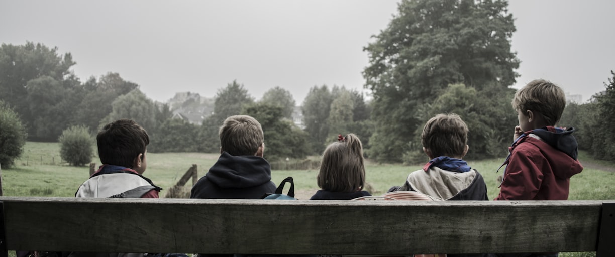 five children sitting on bench front of trees