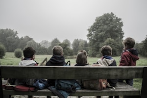 five children sitting on bench front of trees