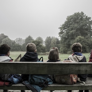 five children sitting on bench front of trees