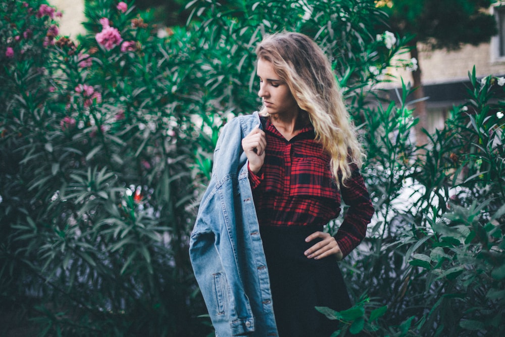 woman holding blue denim jacket standing near green leafed plants