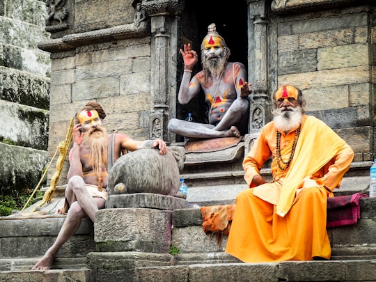 three monks sitting on concrete temple during daytime in Shree Pashupatinath Temple Nepal