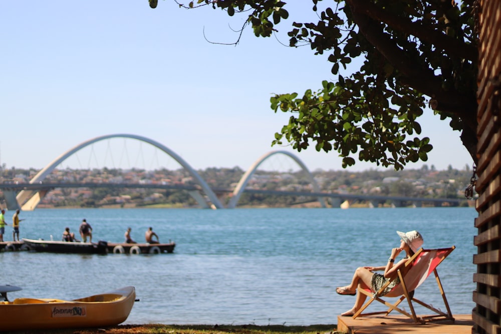 person sitting on pool chair in front of sea with white suspension bridge