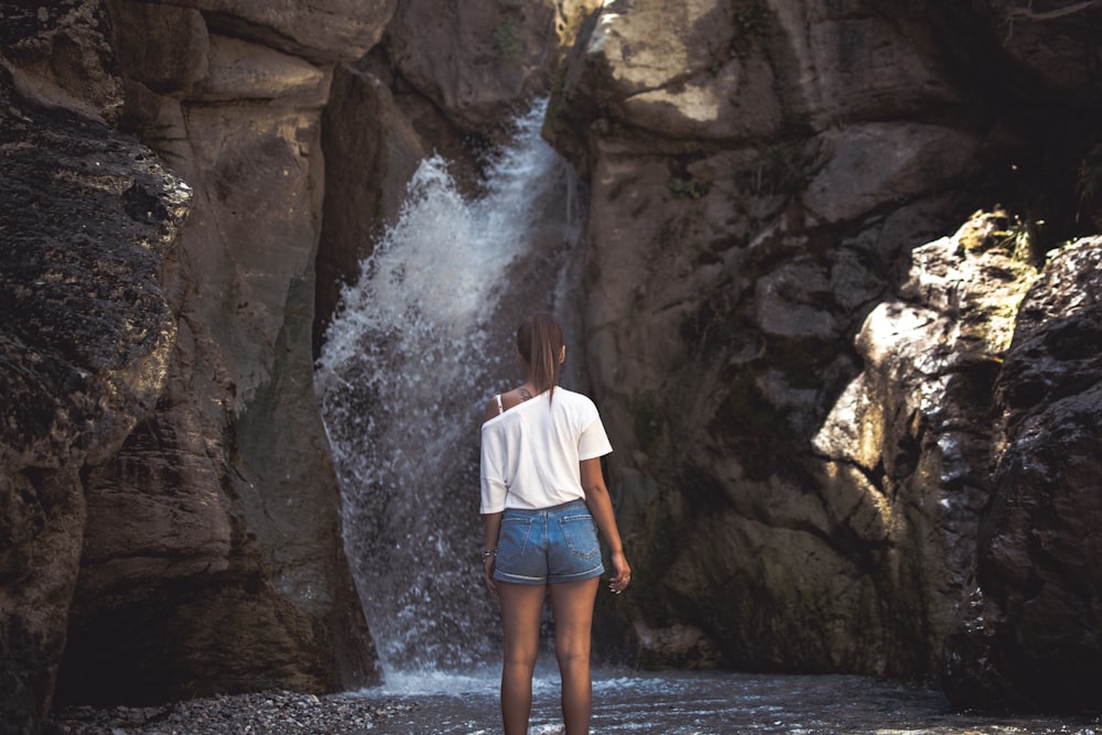 woman in white shirt standing in front of falls