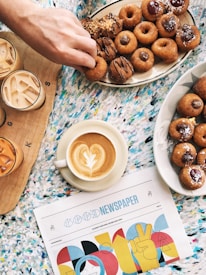 Close-up of a steaming cup of coffee beside a plate of assorted donuts.