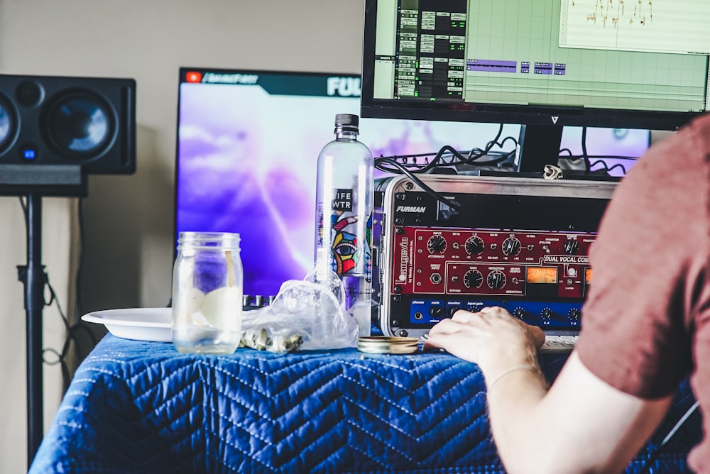 person using computer beside clear glass bottle and jar on blue tablecloth