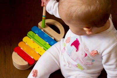 A toddler playing joyfully with colorful wooden toys on a light wooden floor.