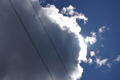 A large, dark cloud partially covers the sun, with rays of sunlight creating a bright, white and slightly iridescent outline around the edges. The sky is a deep blue, and there are two parallel power lines crossing the image from the bottom left to the top right.