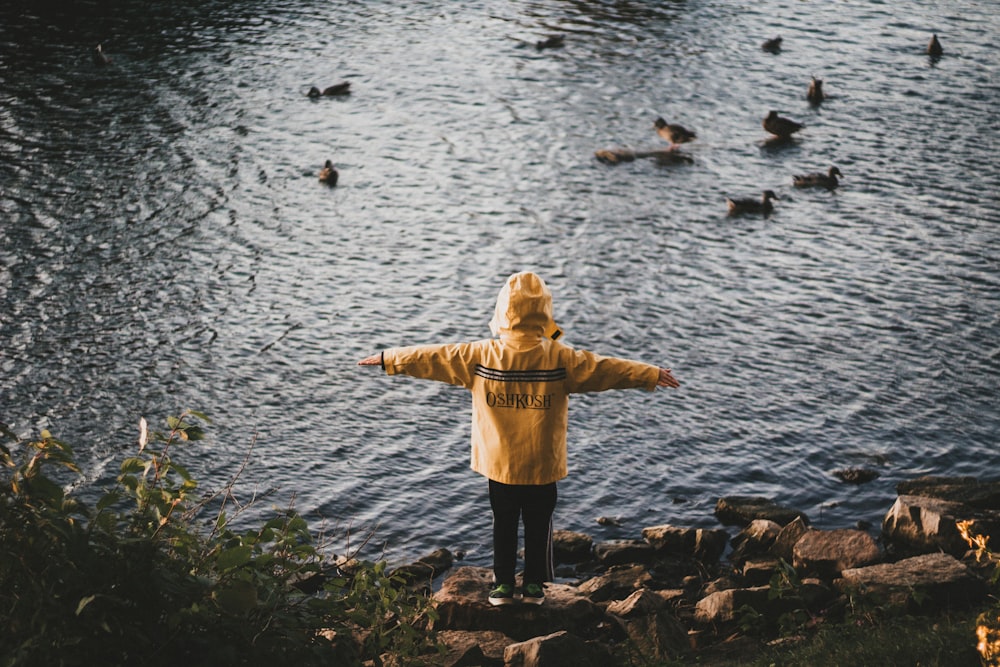 person standing on rock boulder beside body of water