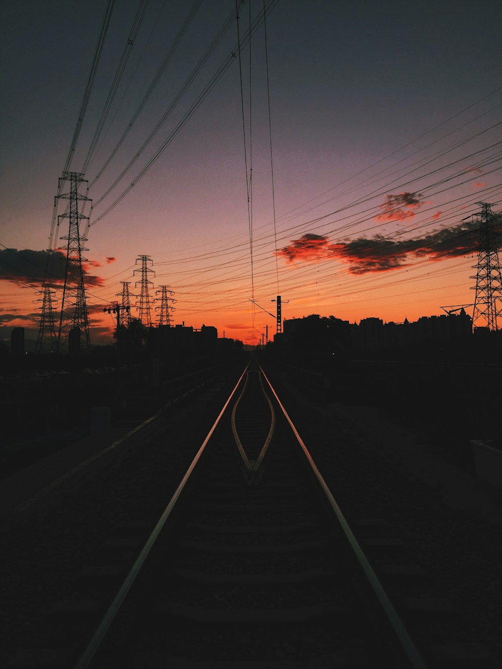silhouette photo of train track under white clouds at golden hour