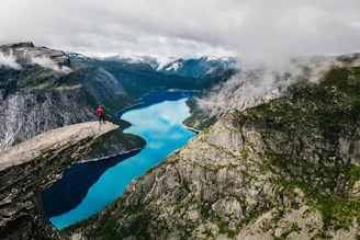 man standing on rock cliff overlooking river near mountain nature photography