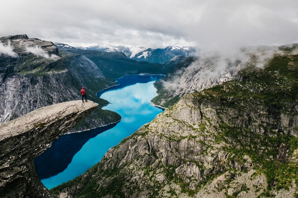 man standing on rock cliff overlooking river near mountain nature photography