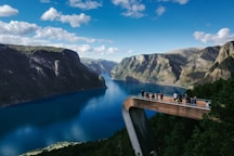 people standing on bridge looking through mountain surrounded by water