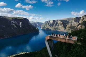 people standing on bridge looking through mountain surrounded by water in Norway