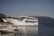 A large white ferry named 'WESTFERRY' with 'CAPTAIN ARISTIDIS' written on its side is docked next to a pier. Smaller boats are moored in the foreground, and a mountainous landscape with sparse vegetation is visible in the background under a clear blue sky.