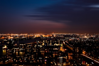 Nighttime panorama of Madrid's skyline with illuminated buildings and the river reflecting lights.