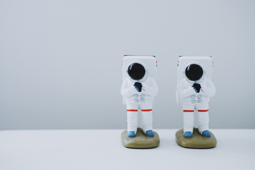 Dos figuritas de traje espacial sobre superficie blanca