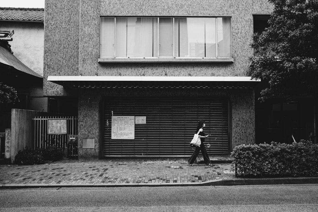 grayscale photo of woman walking beside building