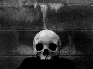 Dark moody close-up of a skull-themed streetwear t-shirt hanging against a black textured wall.