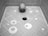 A human skull placed in a tiled shower corner with circular patterns on the floor and a central drain. The tiles are arranged in a geometric pattern.