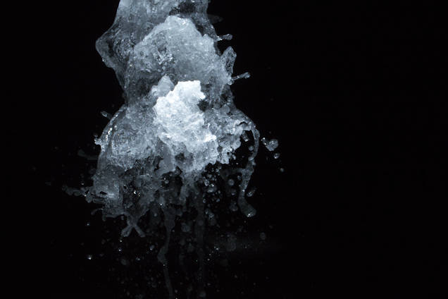 A dynamic splash of water captured in mid-air against a dark background, showcasing intricate and transparent textures with droplets scattering in various directions.