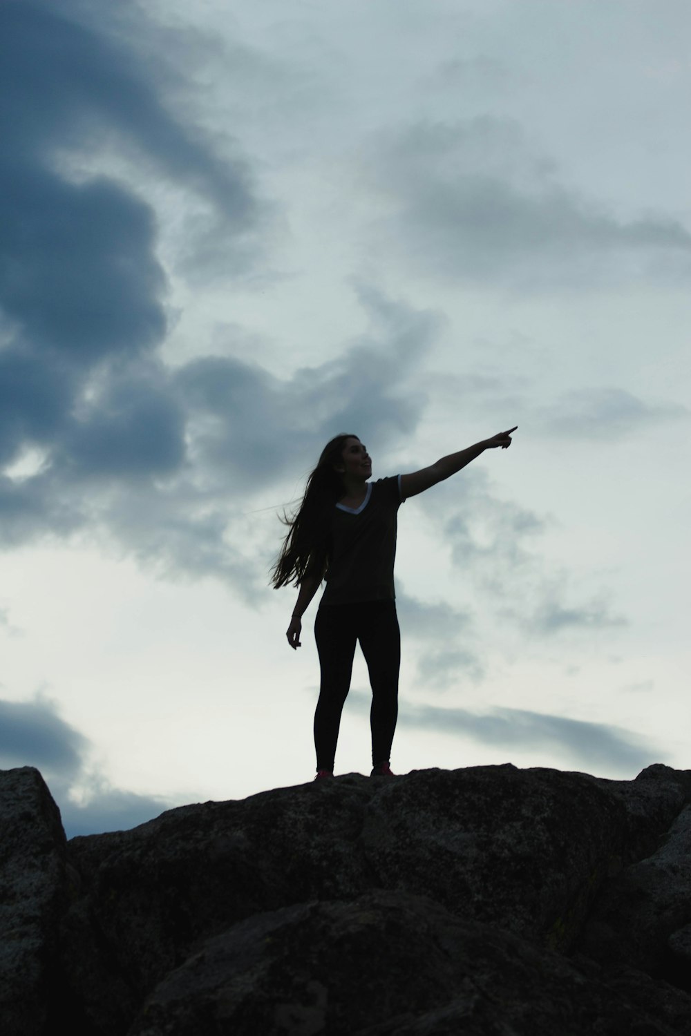 Frau im schwarzen Langarmhemd steht tagsüber auf einem Felsen unter blauem Himmel