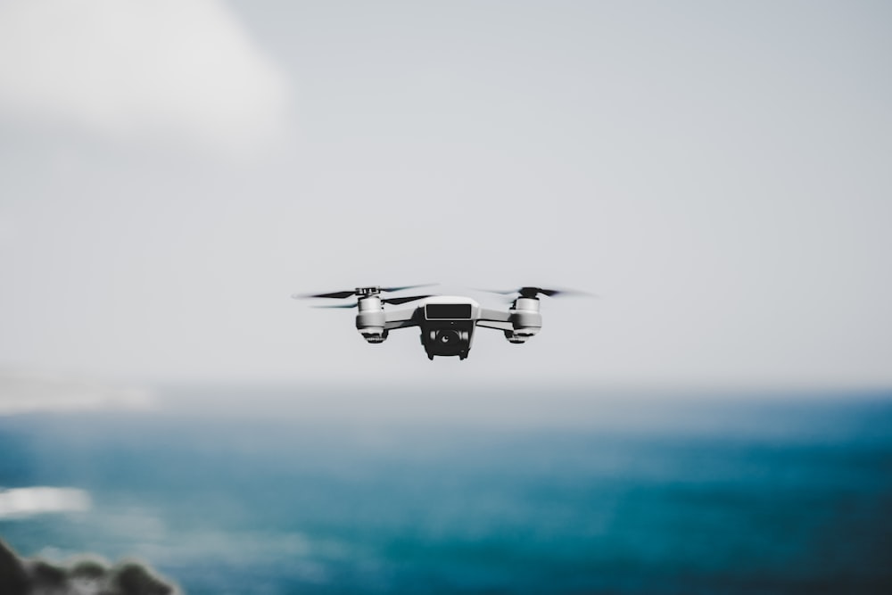 white quadcopter hovering near body of water