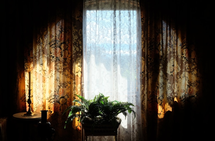 A softly lit living room corner with a plush cream throw draped over a cozy armchair beside a small wooden side table holding a flickering candle and a potted fern.