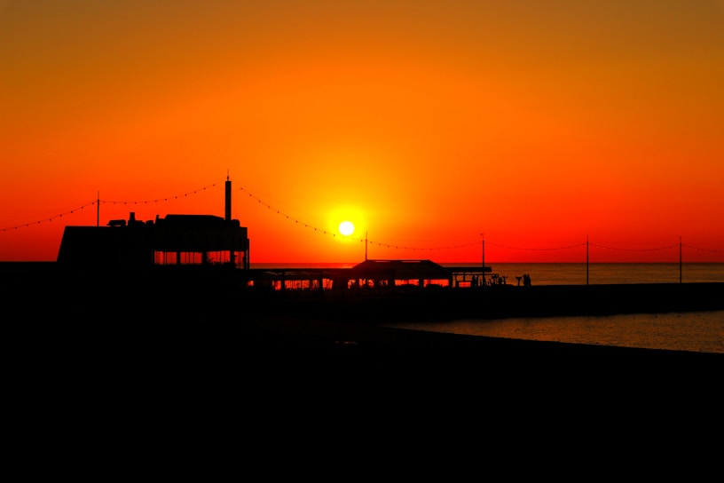 A vibrant vintage poster featuring a sunset over Sarasota beach with warm orange and pink hues.