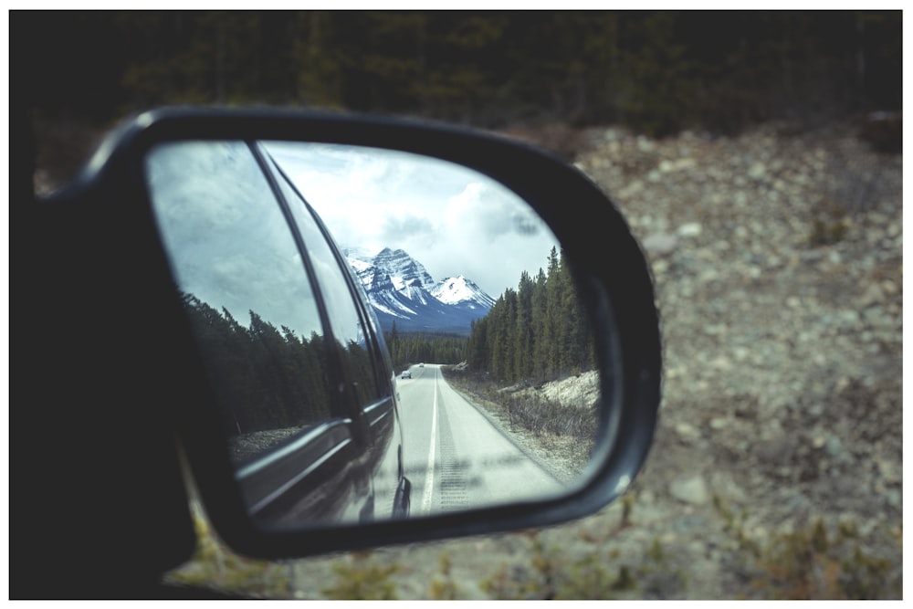 tilt shift photography of side mirror reflecting snow capped mountain