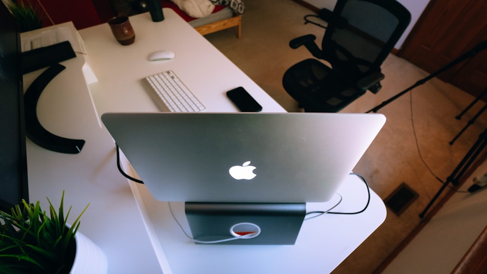 silver MacBook on desk in front of chair
