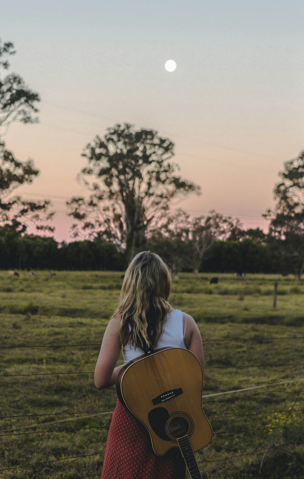 una mujer sosteniendo una guitarra en un campo