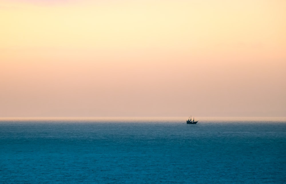 silhouette of boat sailing under cloudy sky during daytime