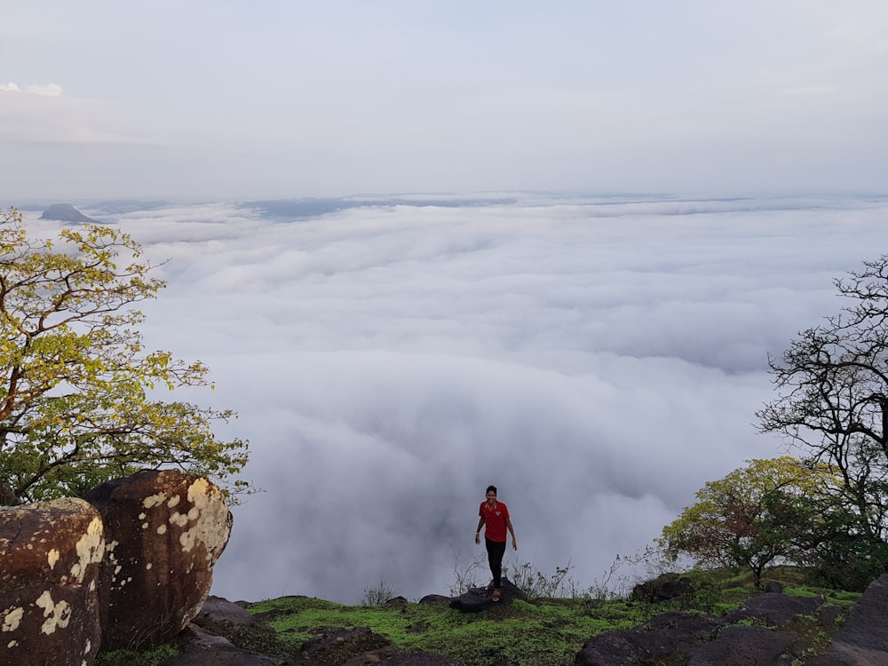 Persona de pie en la cima de la montaña cerca de las nubes blancas con los árboles durante el día