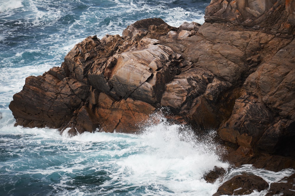 waves crashing on rock at cliff during daytime