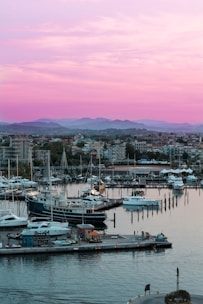 Aerial view of a serene marina with luxury yachts docked along wooden piers at sunset.
