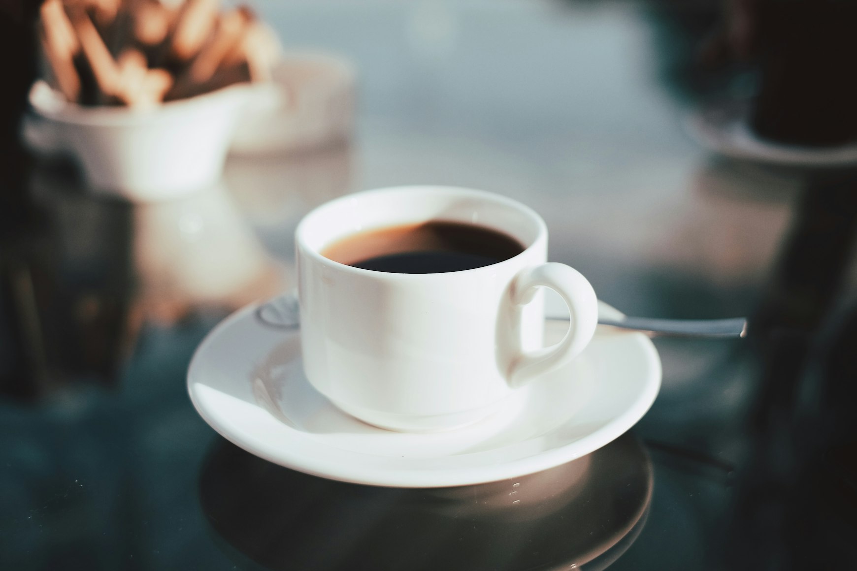 Coffee within a mug, resting on a saucer alongside stirring spoon