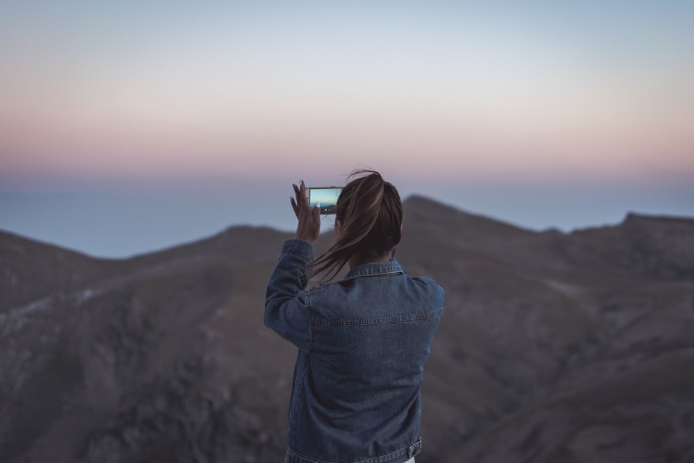 Mujer en chaqueta de mezclilla azul tomando foto de la montaña