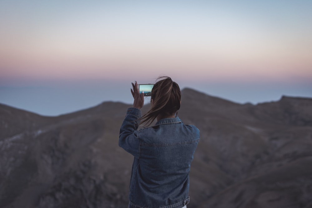 femme en veste en jean bleue prenant une photo de montagne