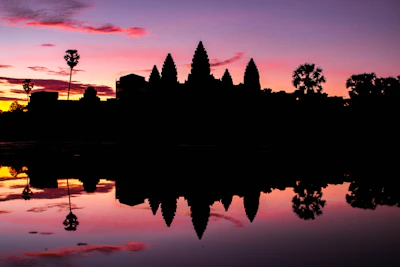 Silhouette of Angkor Wat's towers and trees at dusk (via Unsplash)