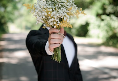 selective focus photo of man wearing black suit jacket holding flower bouquet