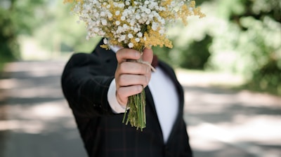 selective focus photo of man wearing black suit jacket holding flower bouquet