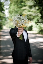 selective focus photo of man wearing black suit jacket holding flower bouquet
