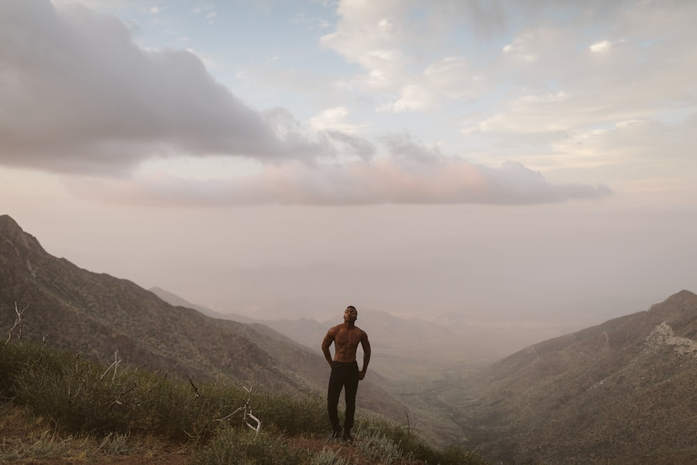 man standing on mountain peak under white clouds