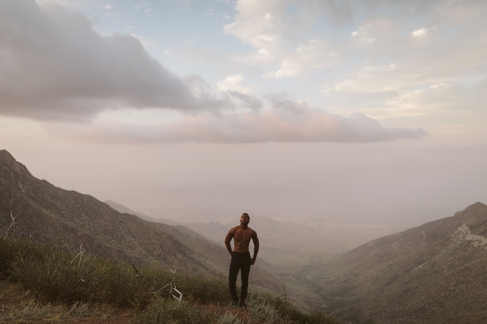 Mann steht auf Berggipfel unter weißen Wolken